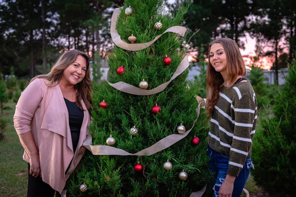 Two women smiling beside a decorated tree in the field at sunset